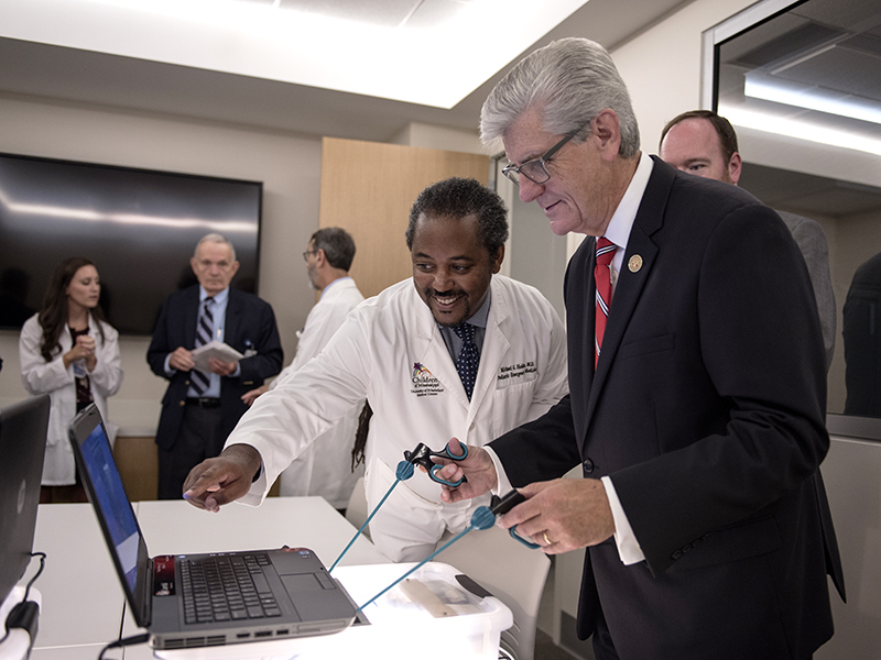 Dr. Michael Holder, left, associate professor of pediatric emergency medicine and executive director of the Office of Interprofessional Simulation, Training, Assessment, Research and Safety, shows Gov. Phil Bryant how to play a game that simulates performance of surgery.